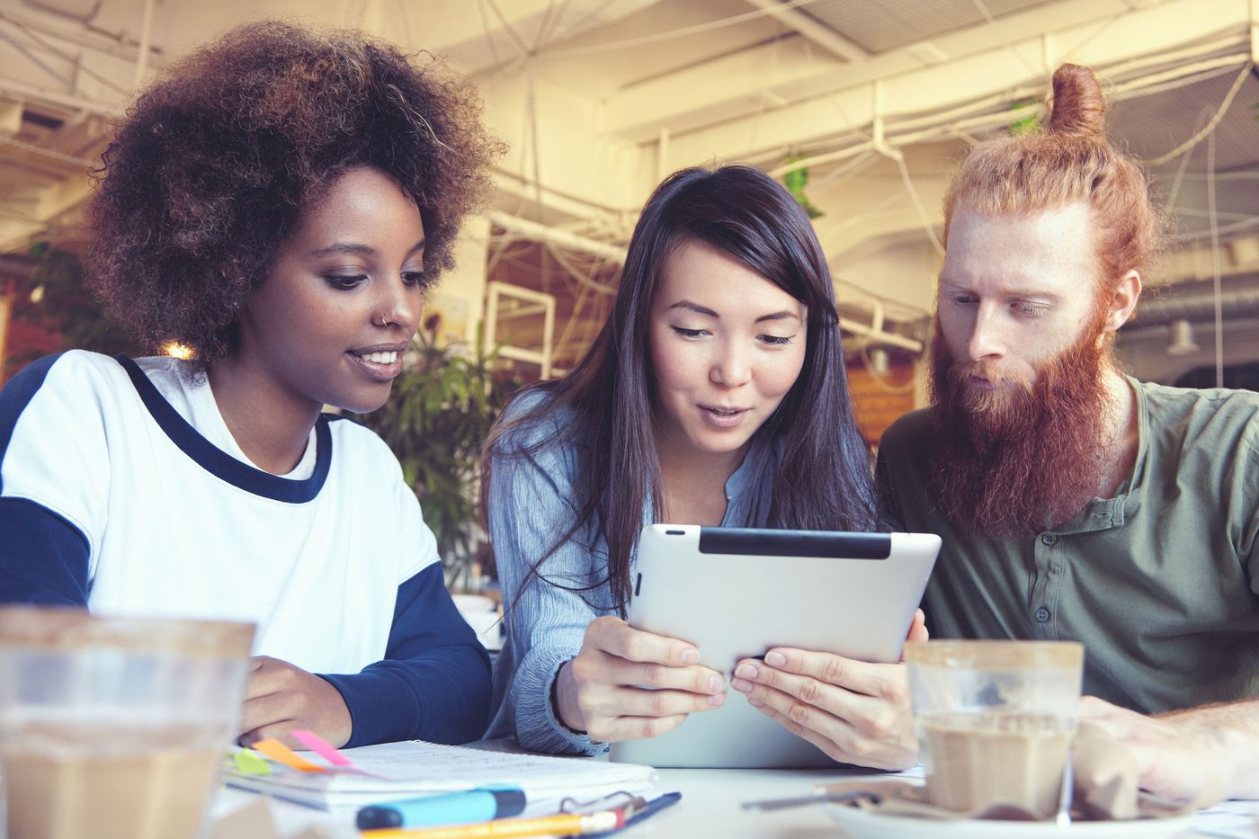 Three people looking at a tablet together in a cafe